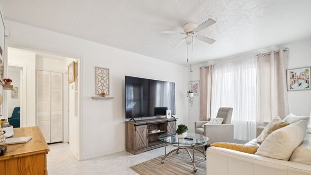A living room with a TV, sofa, and coffee table. There is a wooden cabinet and a ceiling fan.