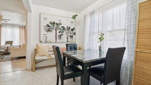 A dining area with a marble table, black chairs, and a painting of palm trees.
