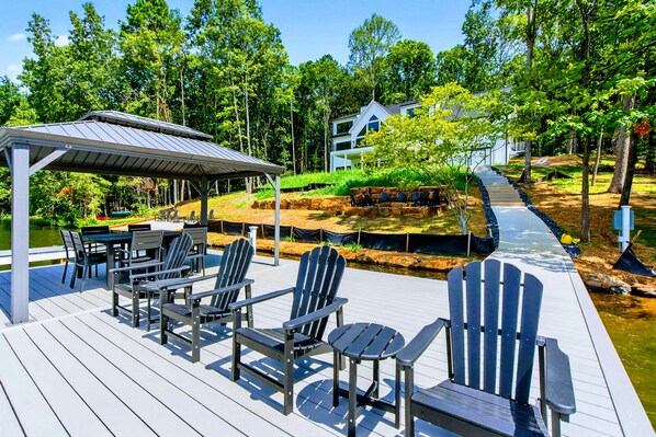 A deck with Adirondack chairs and a covered area, overlooking a landscaped garden and a house.