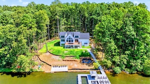 Une maison moderne à deux étages, dotée d’une terrasse et entourée d’une forêt dense, avec un quai donnant sur l’eau.