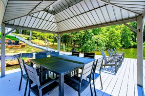 Een overdekt terras buiten, met een tafel en stoelen, met uitzicht op water en groen.