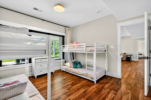 A modern bedroom with bunk beds, a desk, and a window with a view of greenery.