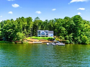 A lakeside property with a two-story house, dock, and surrounding forest.