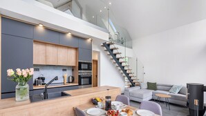 Een moderne keuken met een centraal eiland, een eethoek met een houten tafel, en een trap die naar een hoger niveau leidt.