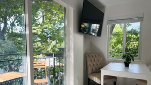 A modern living room with a sliding glass door leading to a balcony, a flat-screen TV mounted on the wall, a small table with a potted plant, and a comfortable armchair. - 0.3 Miles to Space Needle! 2Br/2Ba Belltown Condo w/ Free Garage Parking + AC (Seattle)