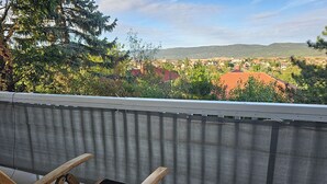 A balcony with a wooden chair and a view of a residential area with houses and hills in the distance. - Bright house with garden, balcony, panoramic view and fully equipped kitchen. (Pilisvörösvár)
