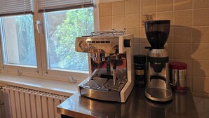 A coffee machine, grinder, and a container on a kitchen counter near a window. - Bright house with garden, balcony, panoramic view and fully equipped kitchen. (Pilisvörösvár)