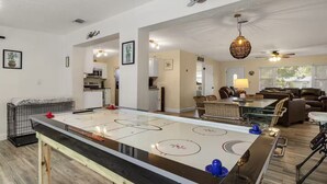Un vaste espace de vie comprenant une grande table de hockey sur glace, un coin repas avec une longue table, et un espace salon confortable avec des canapés et des fauteuils.