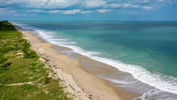Une plage aux eaux turquoise et limpides, bordée d’un rivage sablonneux.