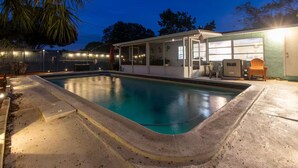 Une piscine avec un patio couvert, du mobilier d’extérieur et une vue sur les arbres environnants.
