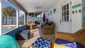 Un espace extérieur abrité, aménagé avec des meubles en osier, une piscine et un panneau indiquant : « Le paradis des tongs ».