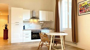 Eine moderne Küche mit weißen Schränken, einem eingebauten Backofen und einem Essbereich mit rundem Tisch und Korbstühlen.