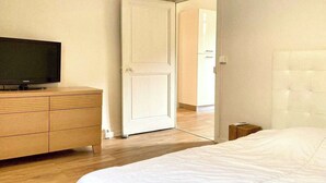 Ein Schlafzimmer mit einem Bett, einem Fernseher auf einer Holzkommode und einer weißen Tür, die in einen anderen Raum führt.