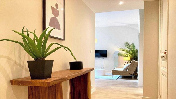 Ein modernes Wohnzimmer mit einer Holzbank, einer Topfpflanze und einem gerahmten Kunstwerk an der Wand.