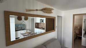 A modern living room with a large mirror, a sofa, and a kitchen area visible through the mirror.