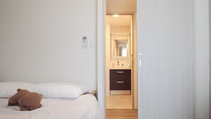 Quarto com cama, um urso de pelúcia, mesa de cabeceira, espelho e banheiro com pia e armário.