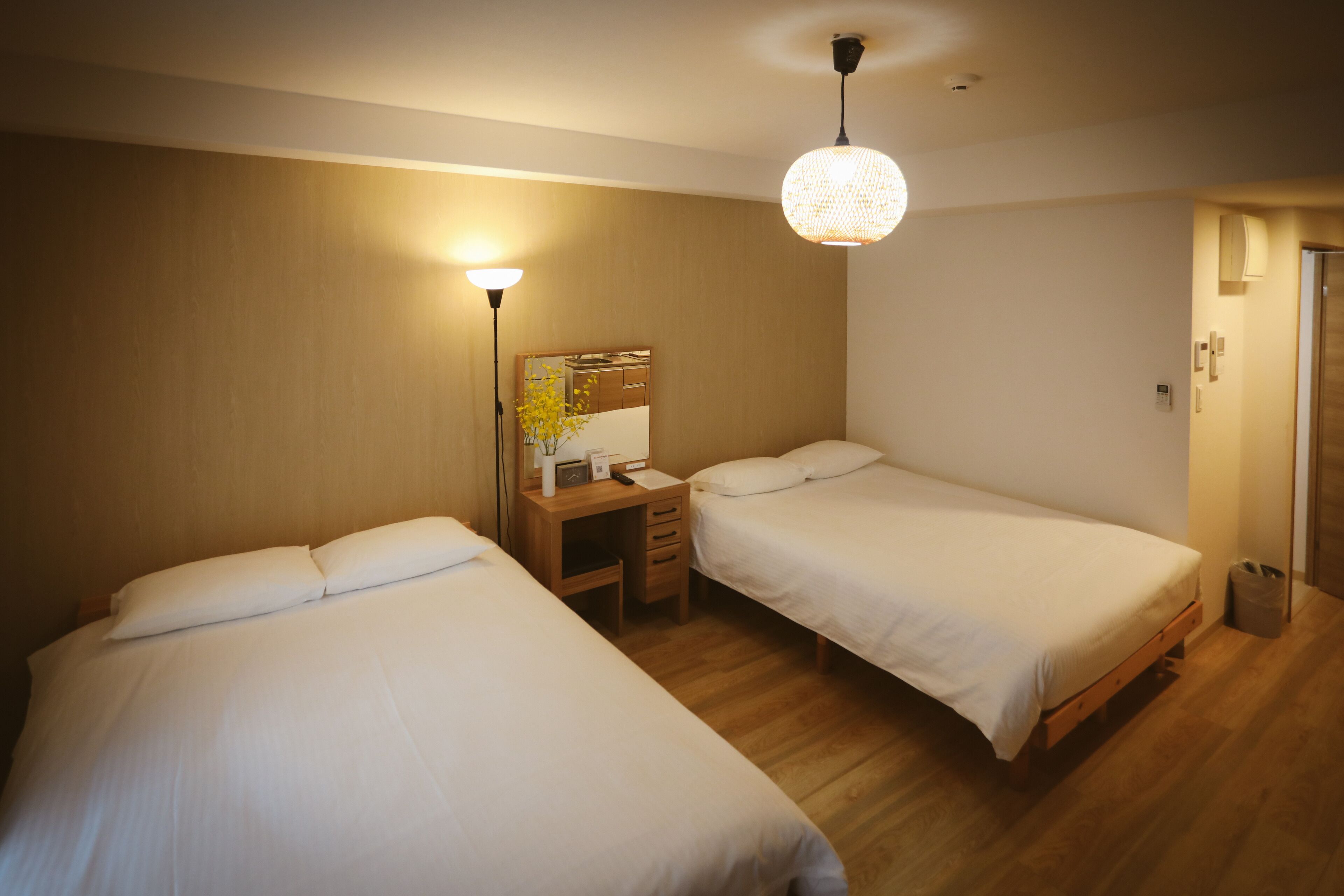 A hotel room with two single beds, a desk with a mirror, and a hanging light fixture.