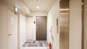 Corredor de hotel com extintor, porta com placa e carpete estampado.