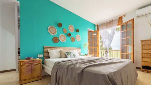 A bedroom with a teal wall, a wooden bed frame, and a large window with curtains. - Corbella by Interhome (Deltebre)