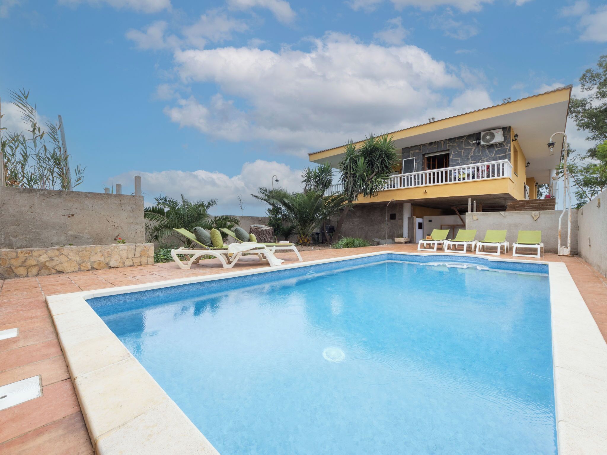 A swimming pool with lounge chairs, a stone wall, and a building with a balcony.