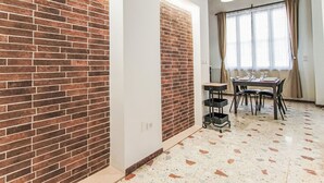 Ein Zimmer mit Backsteinwand, einer Essecke mit Tisch und Stühlen sowie einem Fenster mit Vorhängen.