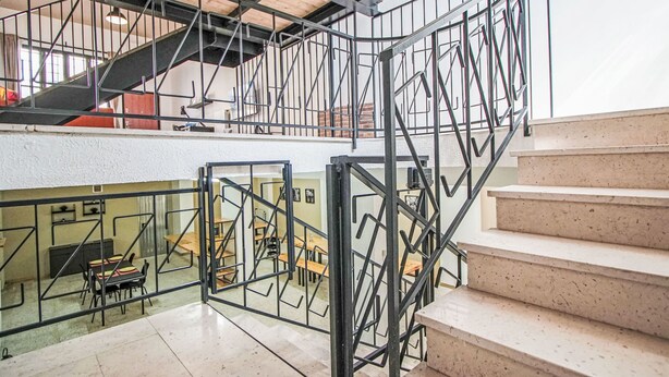 Ein mehrgeschossiges Interieur mit einer Treppe, Metallgeländern und einem Essbereich mit Tischen und Stühlen.