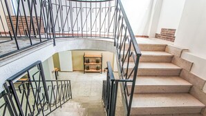 Eine Wendeltreppe mit Metallgeländer, die zu einer niedrigeren Ebene mit einem hölzernen Regal führt, auf dem Flaschen stehen.