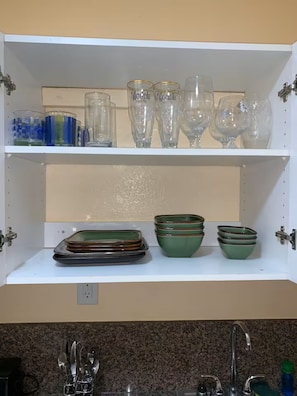 A kitchen shelf with glassware and green bowls.