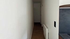 A narrow hallway with white walls and wooden flooring, leading to a door at the end.