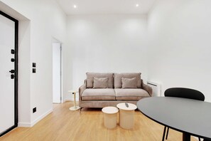 A modern living room with a sofa, two small round tables, a dining table, and a white door.