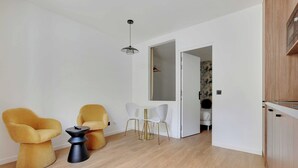 Un espace de vie moderne comprenant un coin repas, deux chaises jaunes, une petite table et un coin cuisine.
