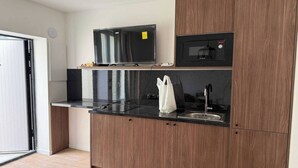 Une cuisine moderne avec un plan de travail noir, des meubles en bois, un four à micro-ondes et un téléviseur.
