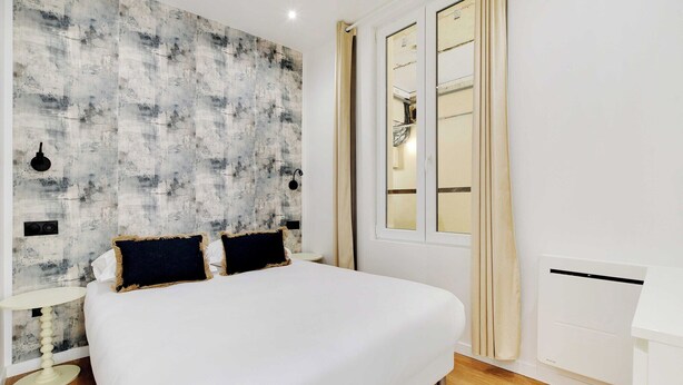 Une chambre à coucher avec un grand lit, un luminaire fixé au mur, une fenêtre avec des rideaux et un radiateur.