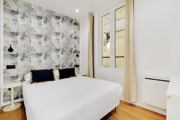 A bedroom with a large bed, a wall-mounted light fixture, a window with curtains, and a radiator.