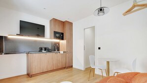 Une cuisine moderne avec des meubles en bois, un four à micro-ondes encastré et un téléviseur à écran plat. On y trouve également un coin repas avec une petite table ronde et des chaises blanches.