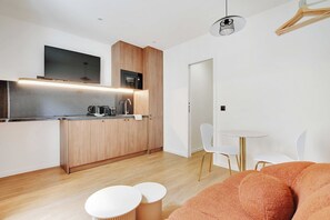 A modern kitchen with wooden cabinets, a built-in microwave, and a flat-screen TV. There is a dining area with a small round table and white chairs.