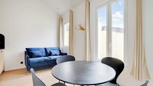 A modern room with a round table, two chairs, a blue sofa, and large windows with curtains.