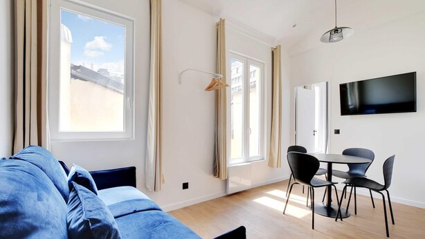 A modern room with a sofa, dining table, chairs, a TV, and large windows with curtains.