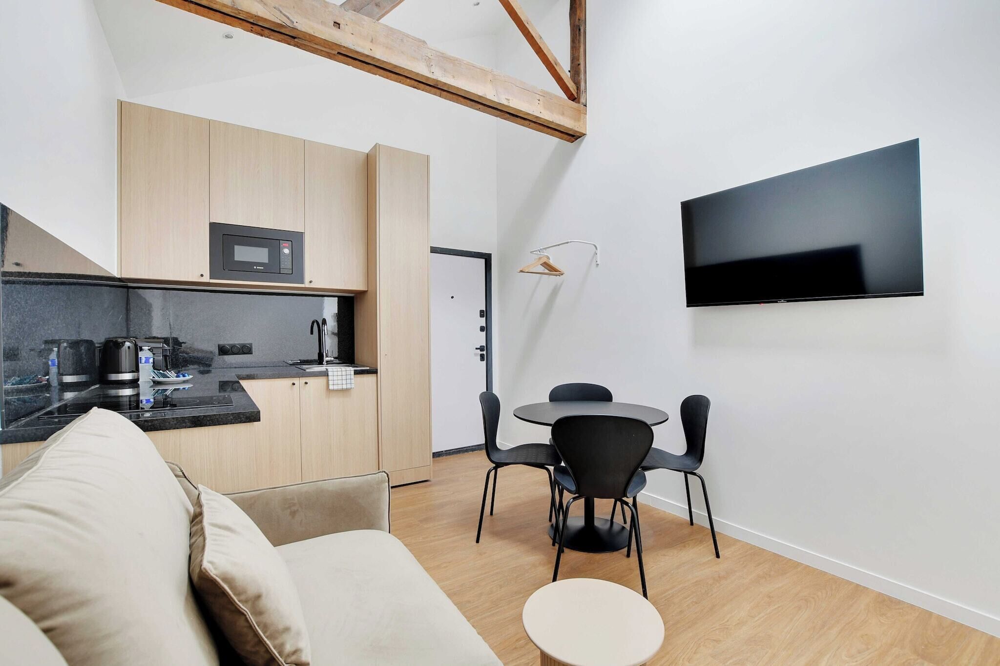 Una cocina moderna con microondas, un comedor con mesa redonda y sillas, y un televisor de pantalla plana montado en la pared.