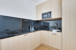 Cozinha moderna com bancada preta, armários de madeira, micro-ondas e cafeteira.