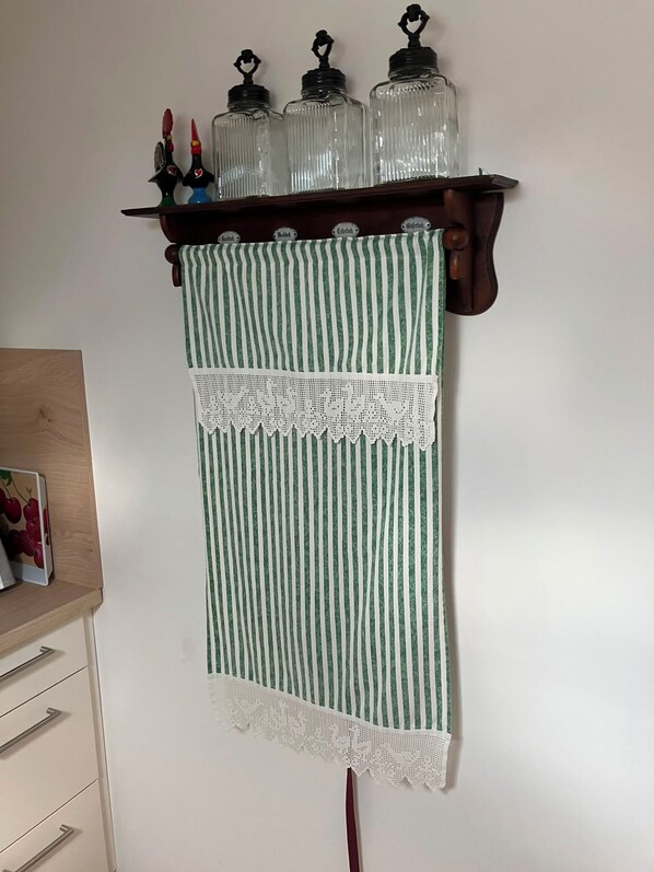 Une cuisine avec une étagère en bois où sont posés des bocaux en verre, un torchon à rayures vertes et blanches, et un meuble en bois orné d’une image de fruits.