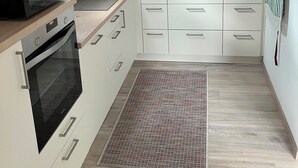 Une cuisine moderne dotée d’une lucarne, d’un four encastré, de meubles blancs et d’un petit tapis.