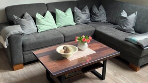 Un salon moderne avec un canapé d’angle gris, une table basse en bois et une lucarne au plafond.