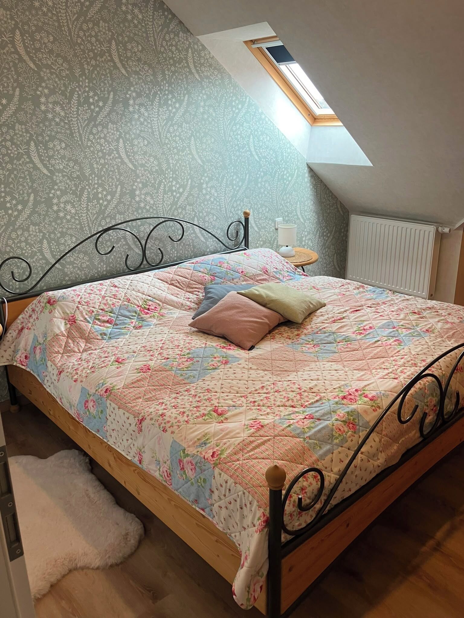 Une chambre à coucher avec un lit, une lucarne, un radiateur et un mur décoré d’un motif.