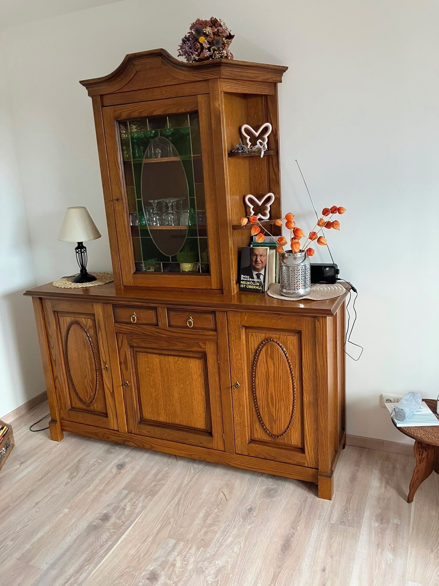 Un meuble en bois avec des portes en verre, une lampe, des objets décoratifs et une petite table sur laquelle est posée une serviette enroulée.