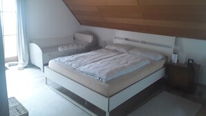 A bedroom with a bed, a chair, a bedside table, and a window with curtains.