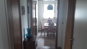 A narrow hallway with a wooden floor leading to a dining area with a table and chairs.