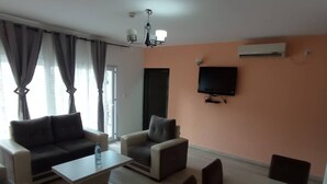 A living room with a sofa, armchairs, a coffee table, and a TV mounted on the wall. - Saint David Hôtel Résidence (Douala)
