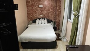 A hotel room with a bed, a dresser, a nightstand, a window with curtains, and a ceiling light. - Saint David Hôtel Résidence (Douala)
