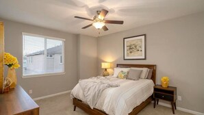 A bedroom with a bed, a ceiling fan, a bedside lamp, a nightstand, a window with blinds, and a framed picture on the wall. - Local 3BD/2.5BA - WiFi & Parking (Carson City)